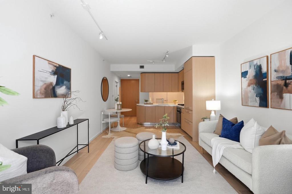 Open-plan living room with a white sofa, blue accent pillow, round coffee table, and light wood kitchen cabinetry.