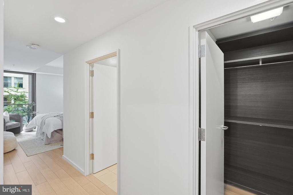 Condo hallway with an open dark wood closet and a bedroom visible beyond.