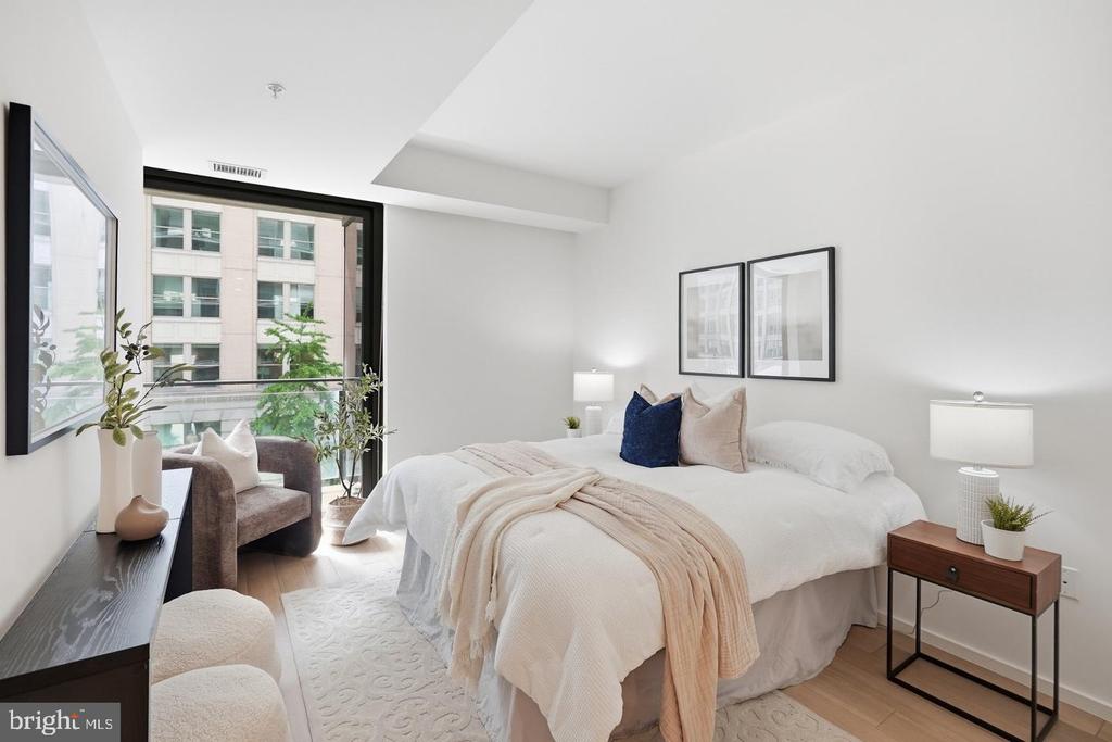 Bright bedroom with a white bed, blush throw, and large windows overlooking neighboring buildings.