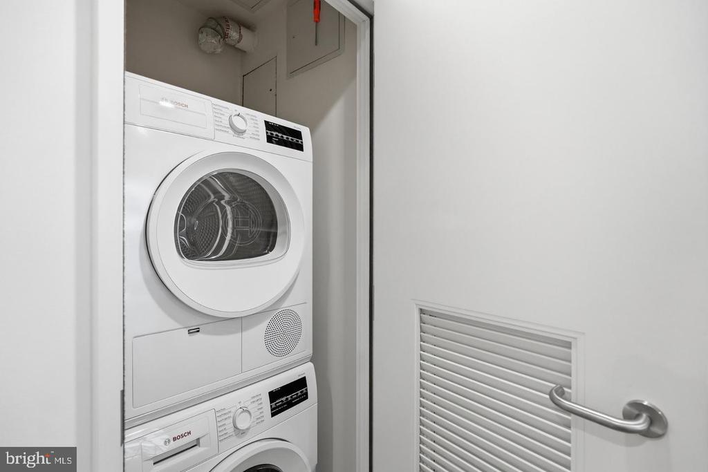 Stacked Bosch washer and dryer in a laundry closet beside a louvered door.