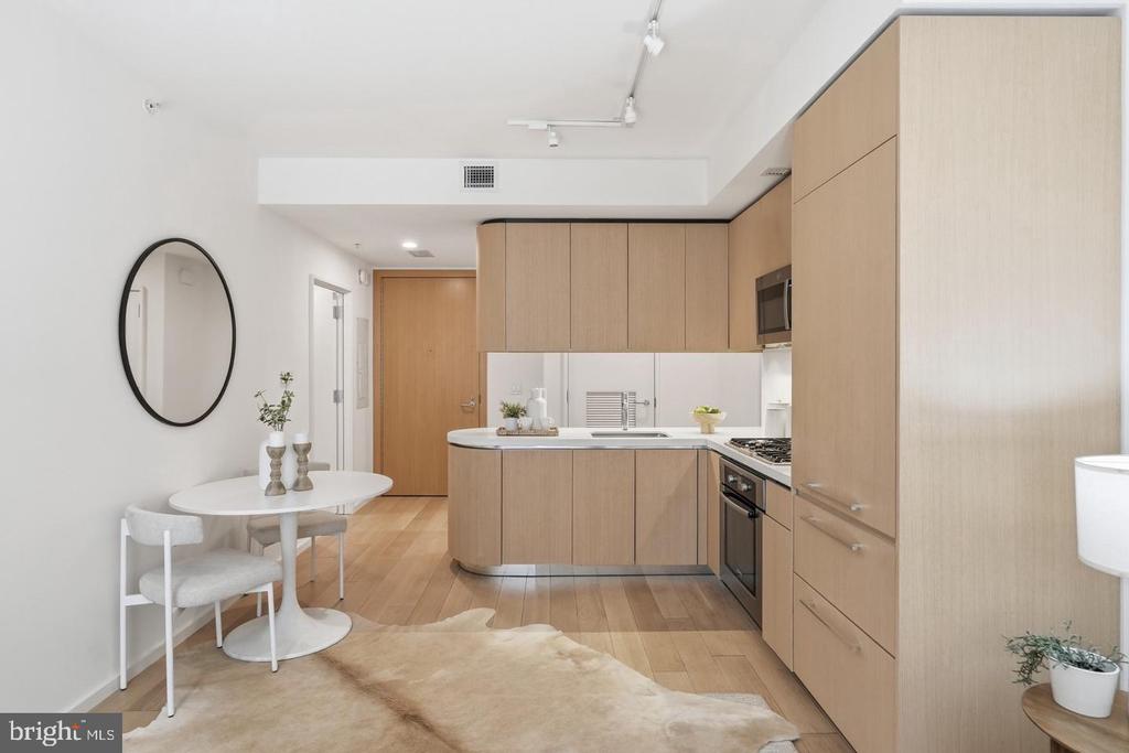 Modern condo kitchen with light wood cabinetry, stainless appliances, and a round dining table.