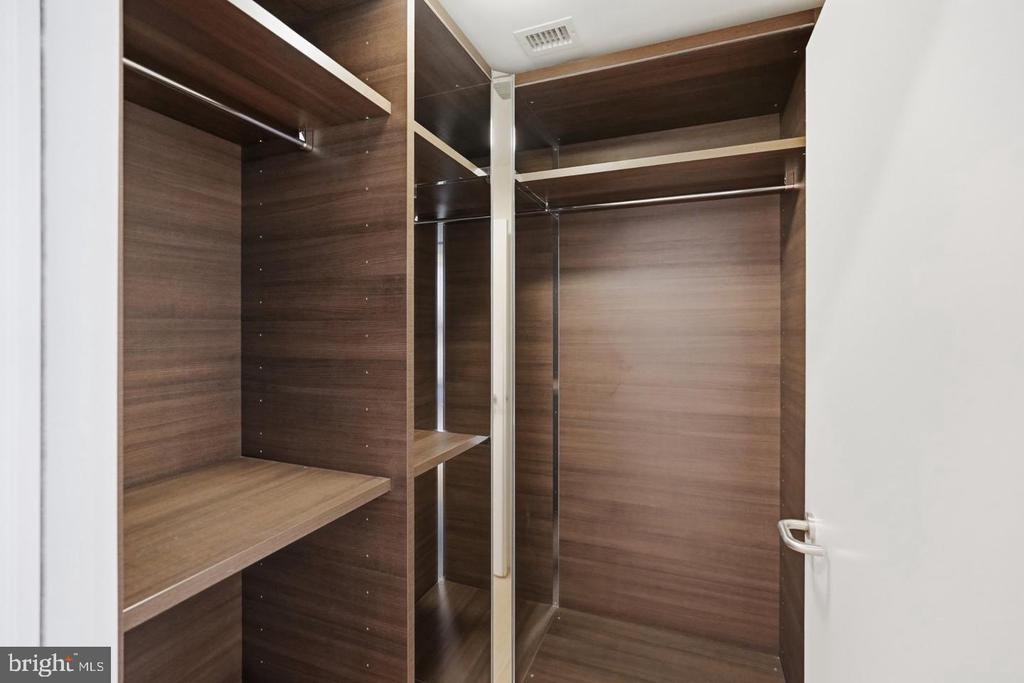 Walk-in closet with dark wood shelving, hanging rods, and a mirrored center panel.
