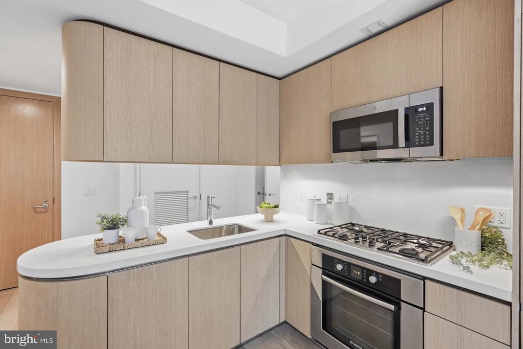 Modern kitchen with light wood cabinetry, white counters, and a stainless steel gas range.