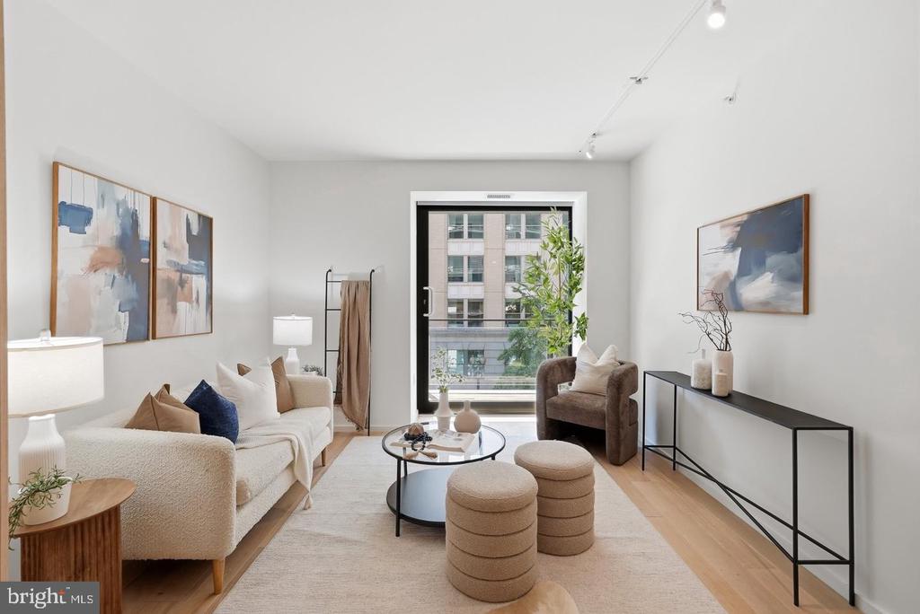 Staged living room with a cream sofa, round coffee table, and large window overlooking a neighboring building.