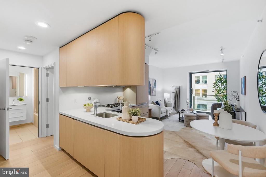 Open-plan condo kitchen with a curved light wood island, dining area, and large living-room windows.