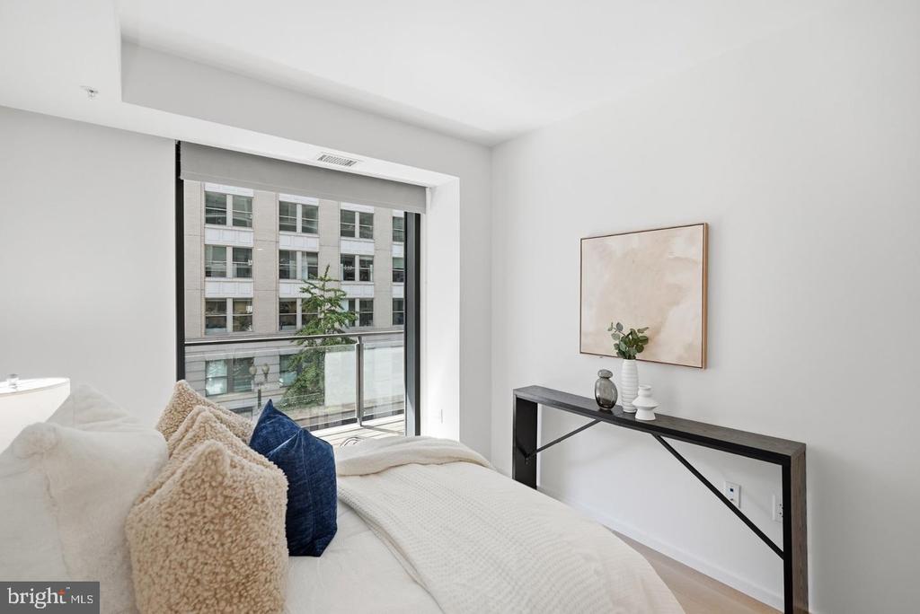 Staged bedroom with a white bed and large window overlooking a neighboring building.