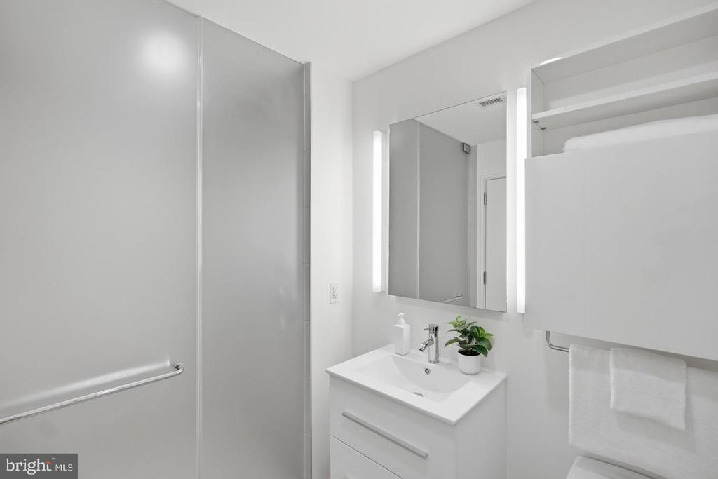 Bathroom with glass shower, illuminated mirror, and white vanity.