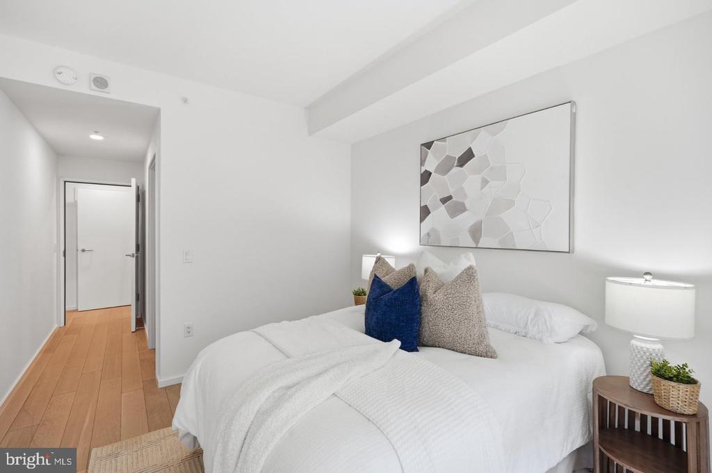 Staged bedroom with a white bed, blue accent pillow, and geometric wall art.