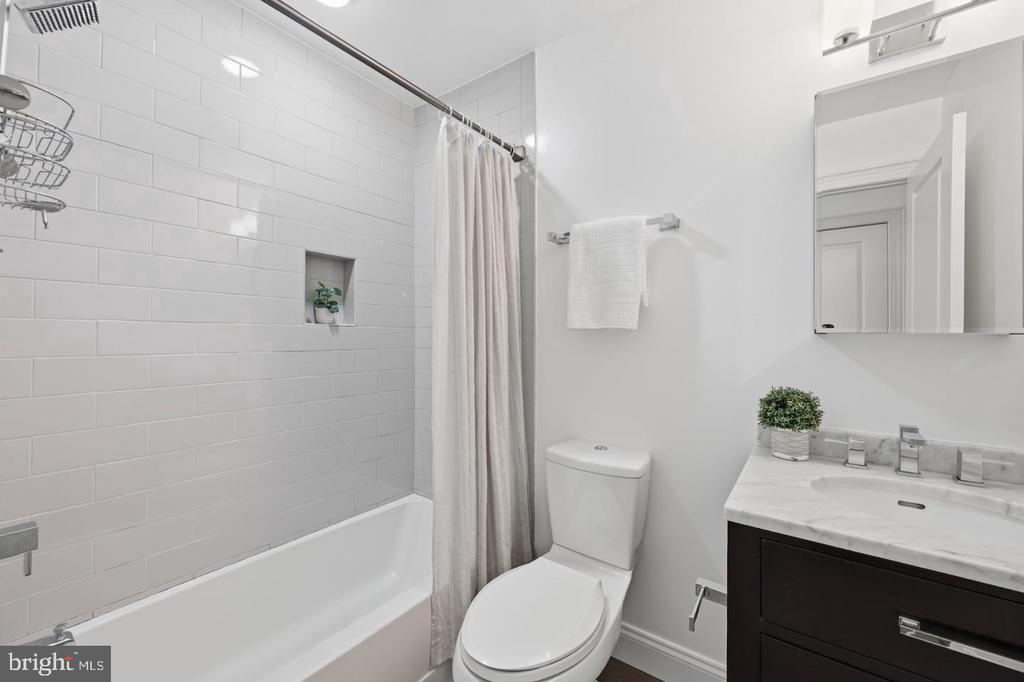 Bathroom with white subway-tile tub surround, shower curtain, toilet, and dark vanity with a marble-look counter.