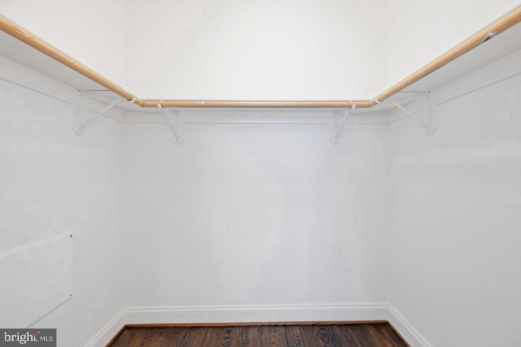 Empty walk-in closet with a wraparound wooden clothes rod and dark hardwood flooring.