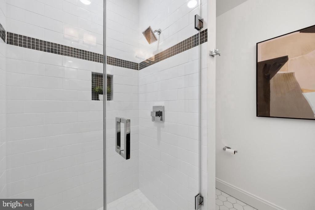 White-tiled bathroom shower with a dark mosaic stripe, chrome fixtures, and glass enclosure.