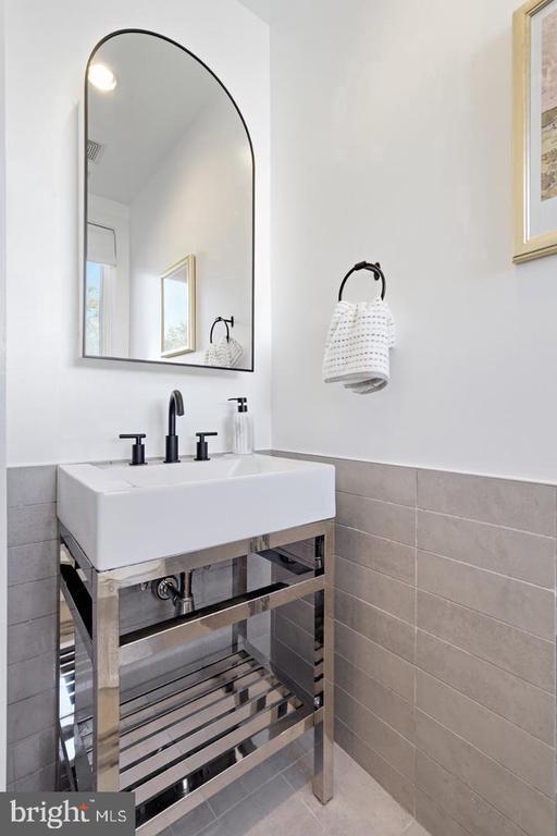 Bathroom with a chrome-frame vanity, white sink, arched mirror, and gray tile.