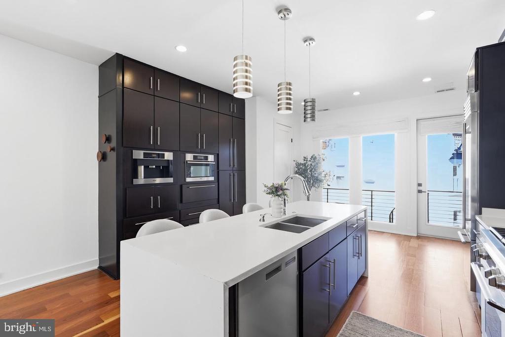 Modern kitchen with a large white island, dark cabinetry, stainless steel appliances, and balcony doors.