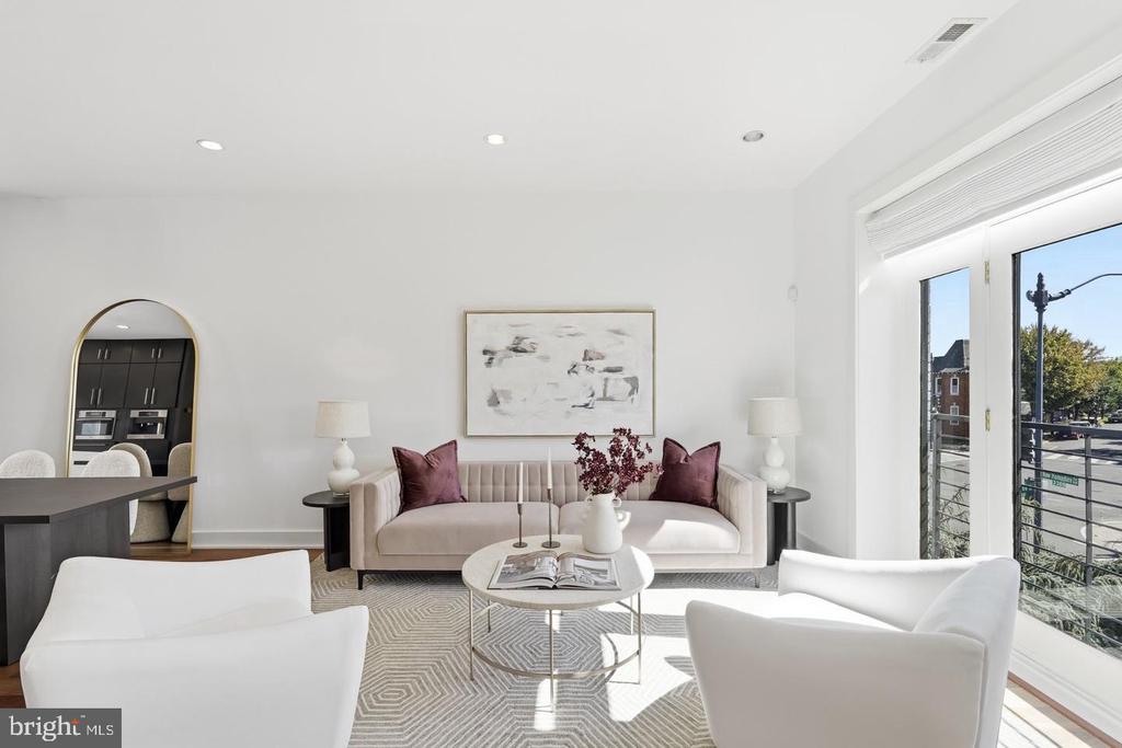 Staged living room with blush sofa, white armchairs, geometric rug, and bright balcony doors.