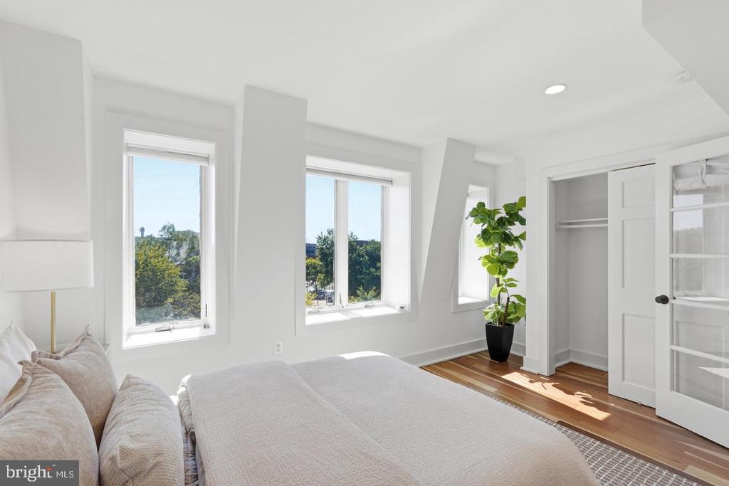 Bright bedroom with a large bed, hardwood floors, tall windows, and an open closet.