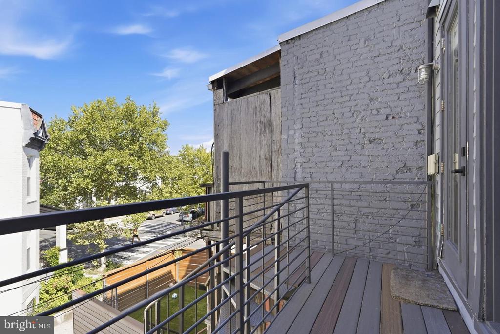 Apartment balcony with gray decking and black railings overlooking a tree-lined residential street.