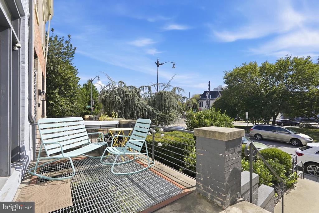 Furnished terrace with pale blue seating and a metal-grid deck overlooking a leafy street.