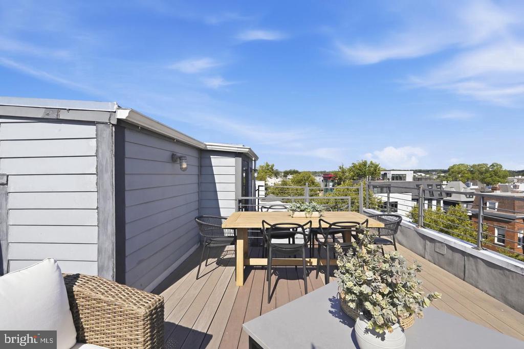 Rooftop deck with outdoor dining and lounge seating overlooking nearby buildings.