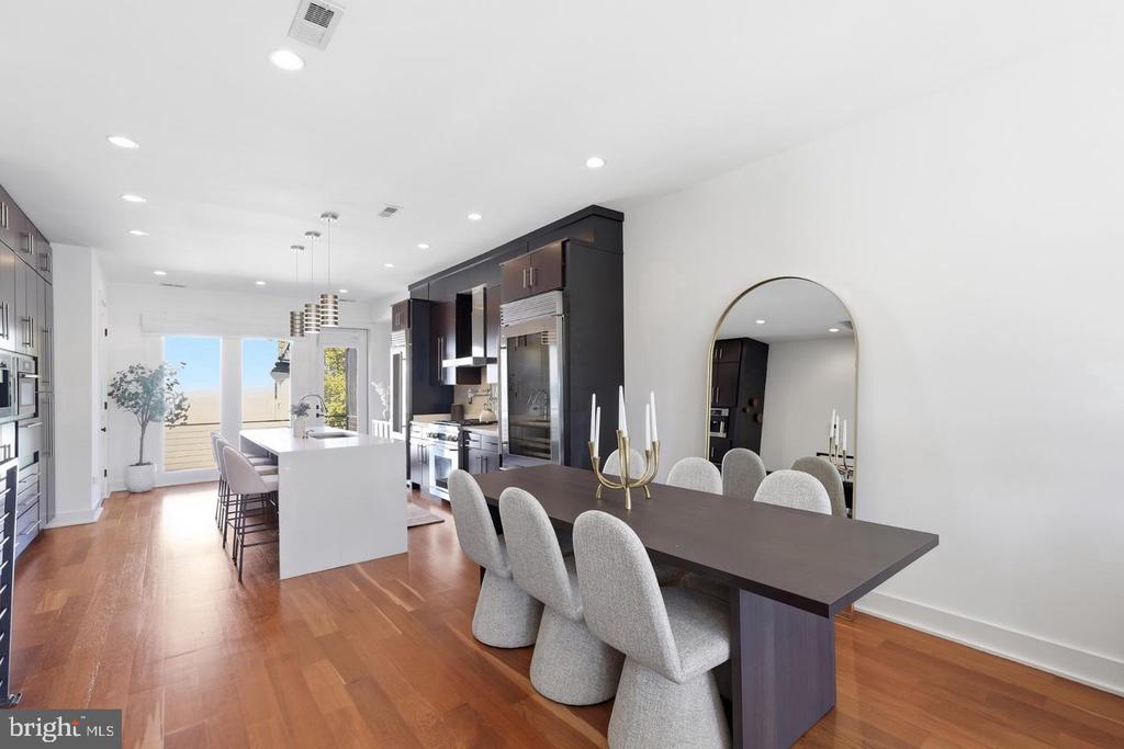 Open-plan kitchen and dining area with dark cabinets, a white island, and a long table beside glass doors.