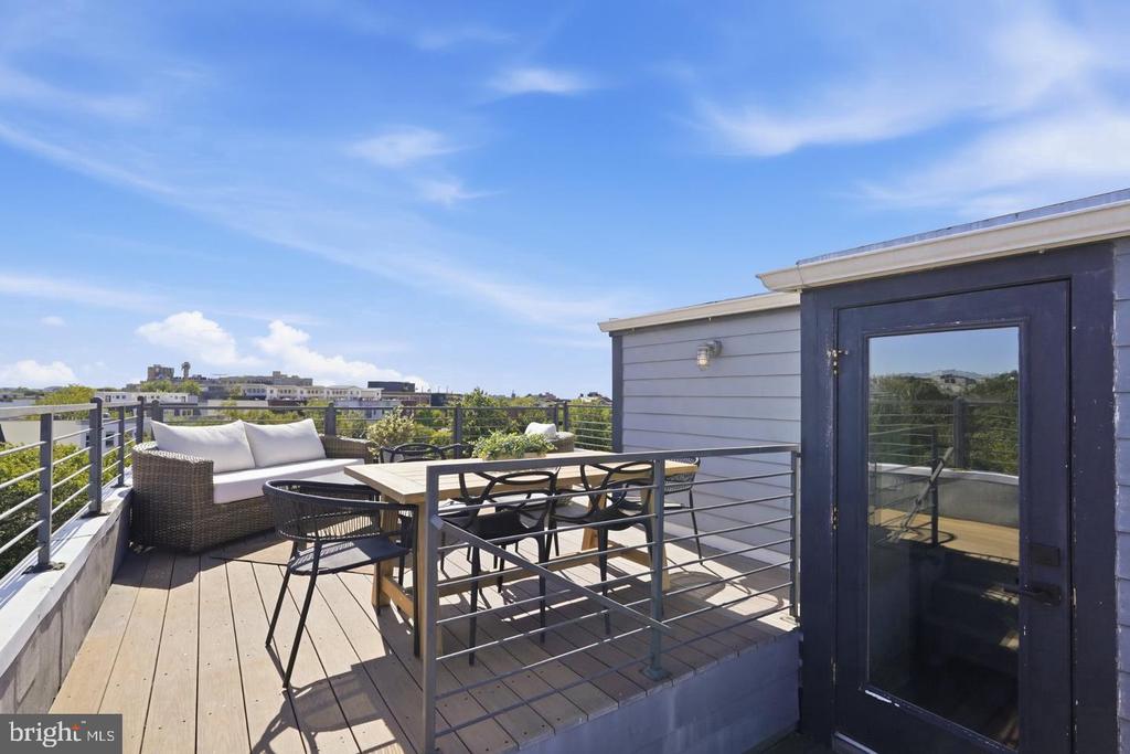Rooftop deck with a dining set, cushioned wicker sofa, and views over surrounding trees and buildings.