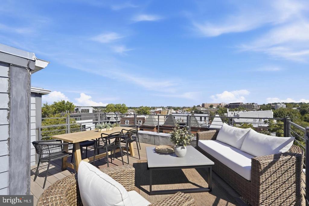 Furnished rooftop terrace with wicker lounge seating, an outdoor dining table, and views across the city.