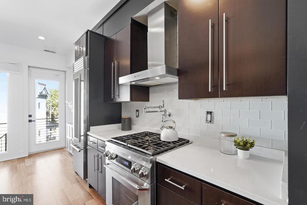 Modern kitchen with dark wood cabinets, stainless steel appliances, and a gas range beside a balcony door.