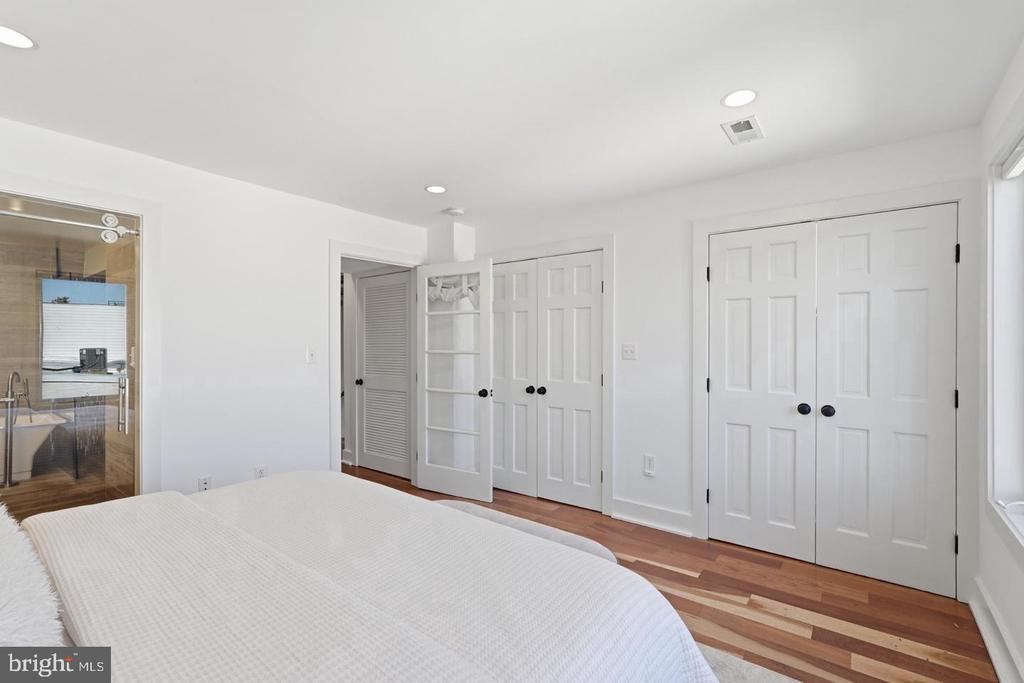 Bedroom with a white bed, hardwood floors, built-in shelving, and double-door closets.