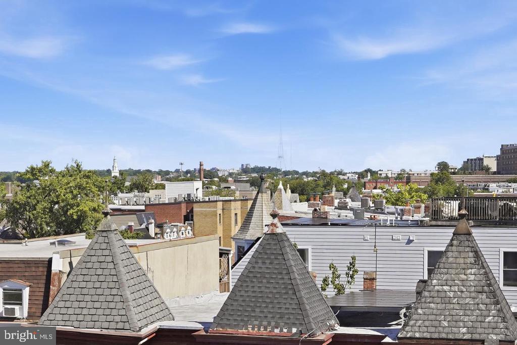City rooftops and slate-shingled turrets seen from above beneath a clear blue sky.