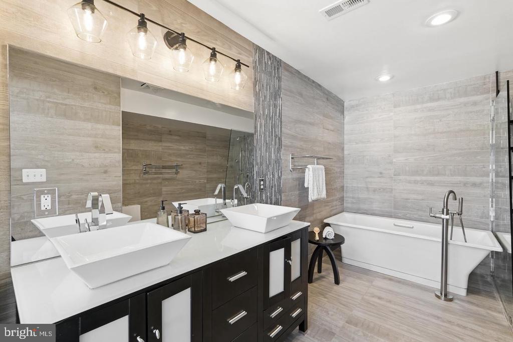 Modern bathroom with double vessel sinks, dark vanity, gray tile and a freestanding tub.