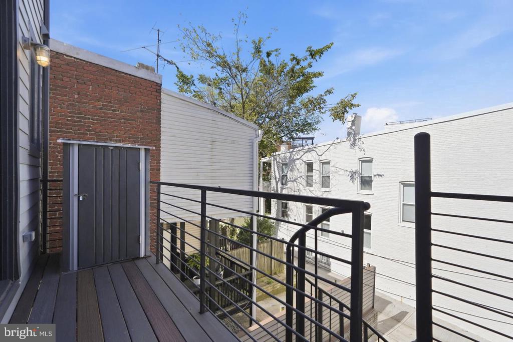 Balcony with dark railings overlooking nearby brick and white-sided buildings.