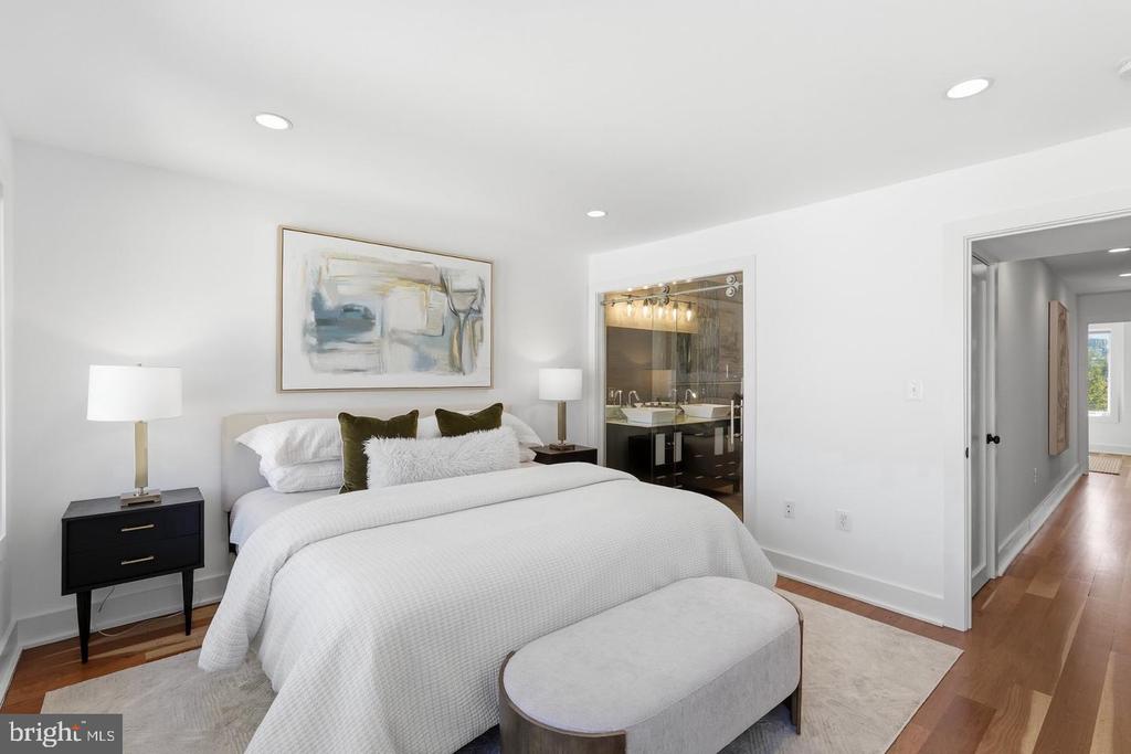 Staged bedroom with a white bed, abstract wall art, and a glass-enclosed bathroom.