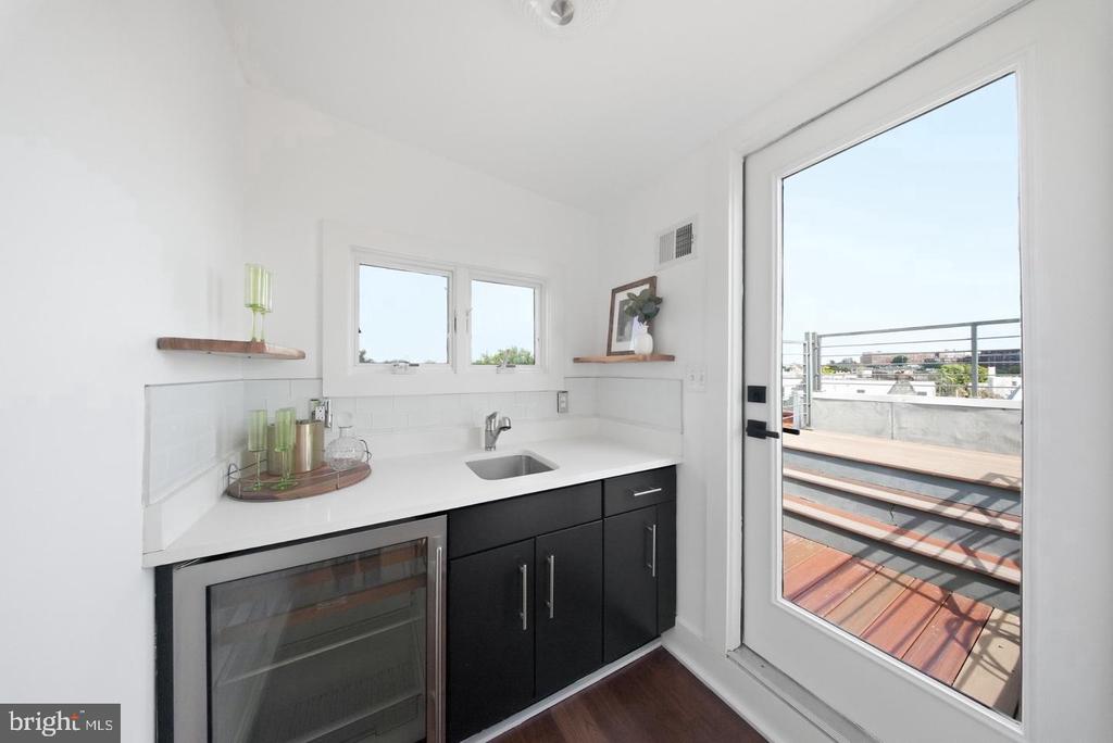 Rooftop wet bar with black cabinets and beverage fridge beside a glass door to the deck.