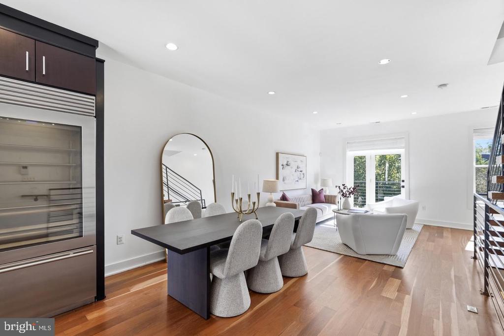 Open-plan dining and living room with hardwood floors, a dark table, and white lounge chairs by glass doors.