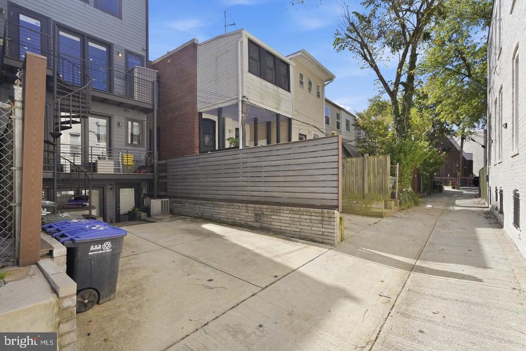 Rear of attached residences along a paved alley, with balconies and a wooden privacy fence.