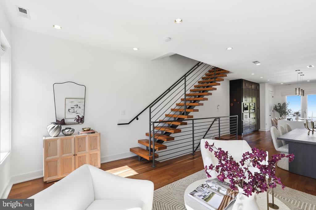 Open-plan living room with white seating, hardwood floors, and a striking wood-and-metal staircase.