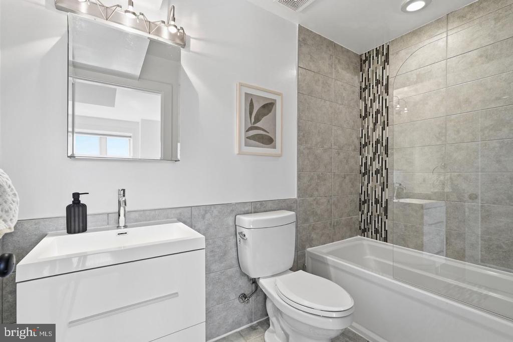 Modern bathroom with white vanity, gray tile, and a tub-shower with a mosaic accent strip.