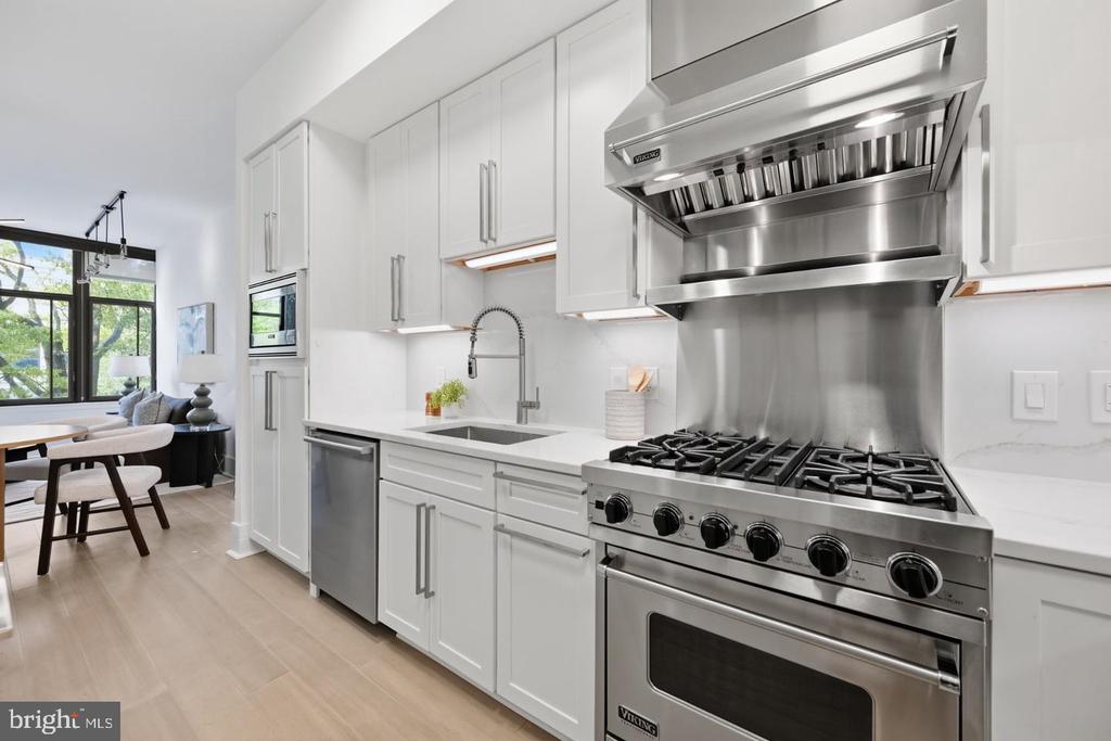 Modern white kitchen with a stainless steel Viking range and oversized vent hood, opening to a window-side sitting area.