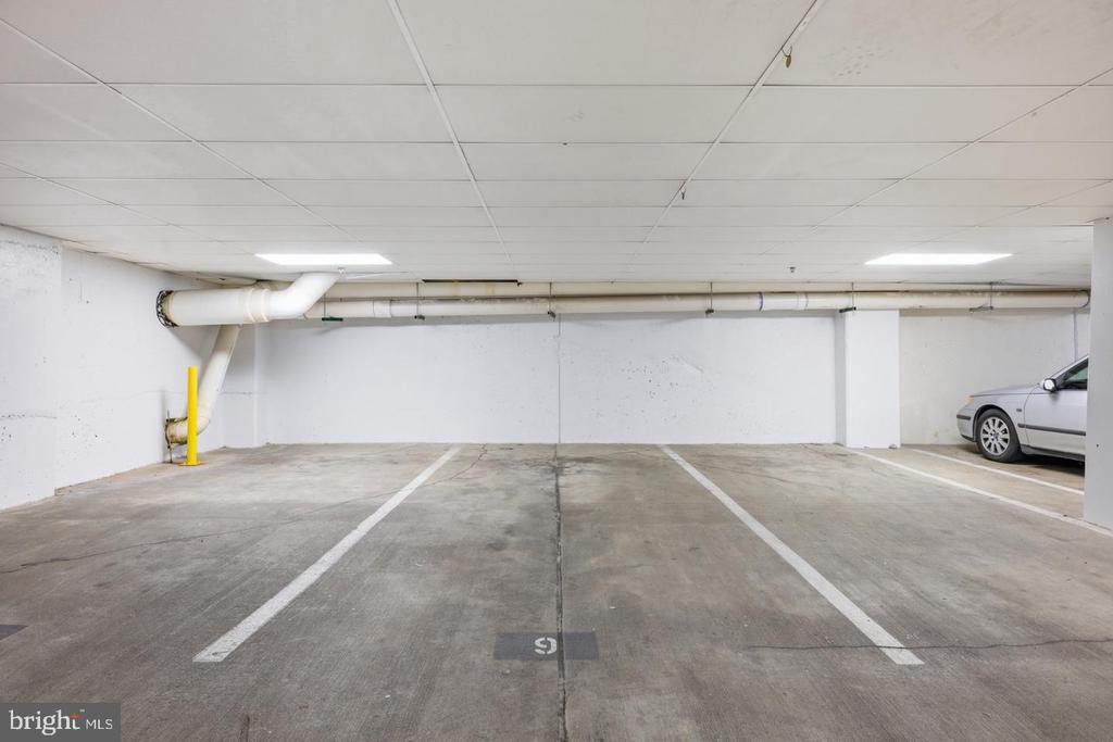 Underground parking garage with marked spaces, exposed pipes, and part of a car.
