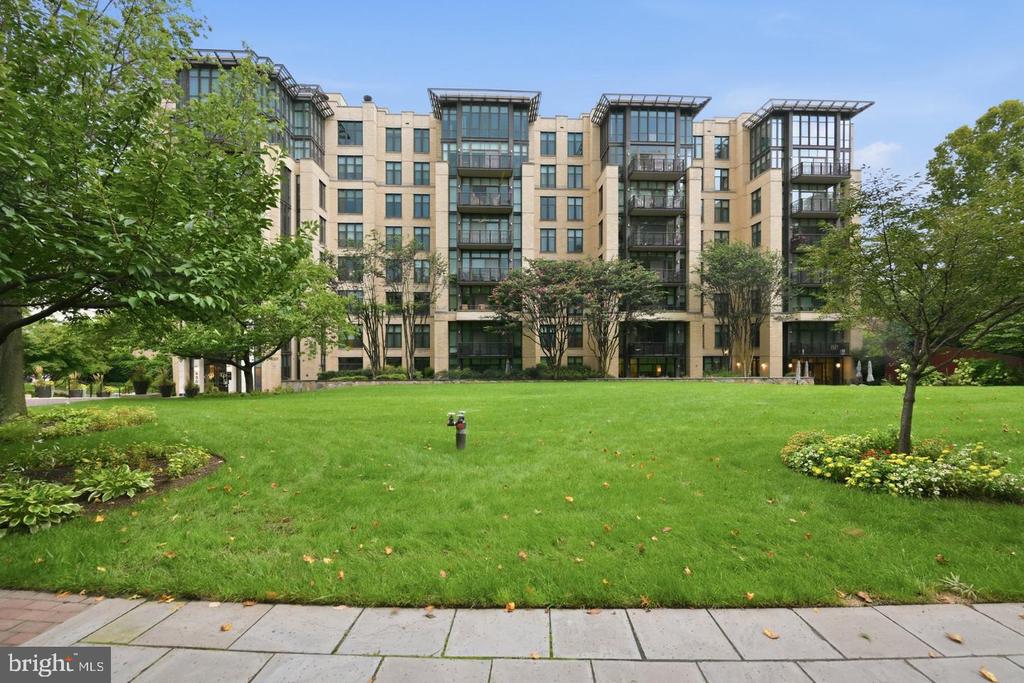 Modern condominium building with glass balconies behind a broad landscaped lawn.