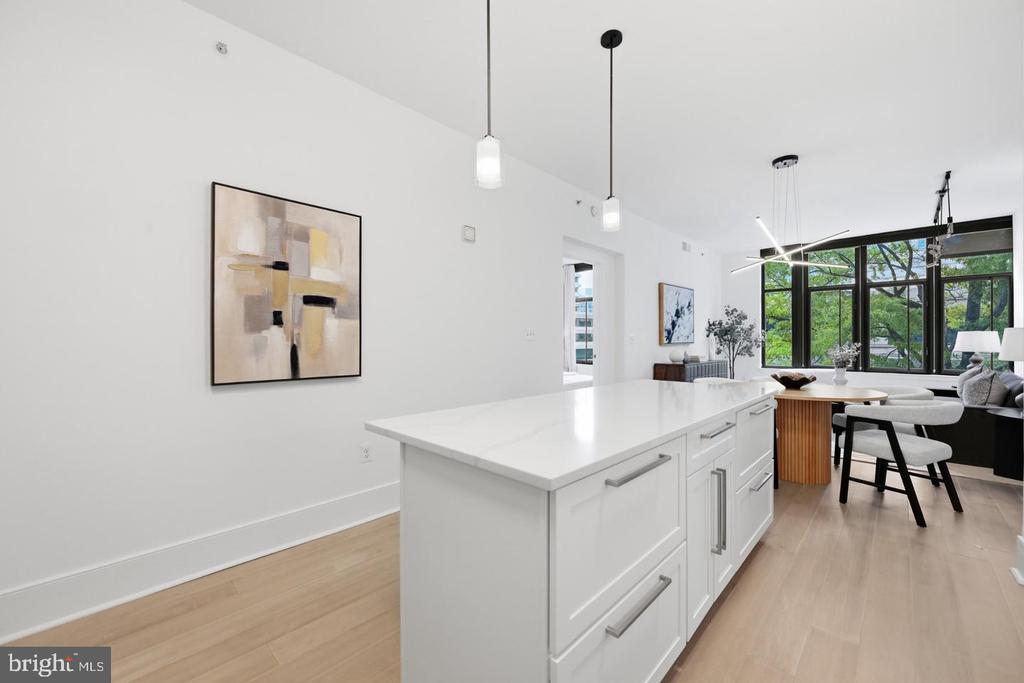 Bright kitchen with a large white island and black-framed windows overlooking leafy trees.