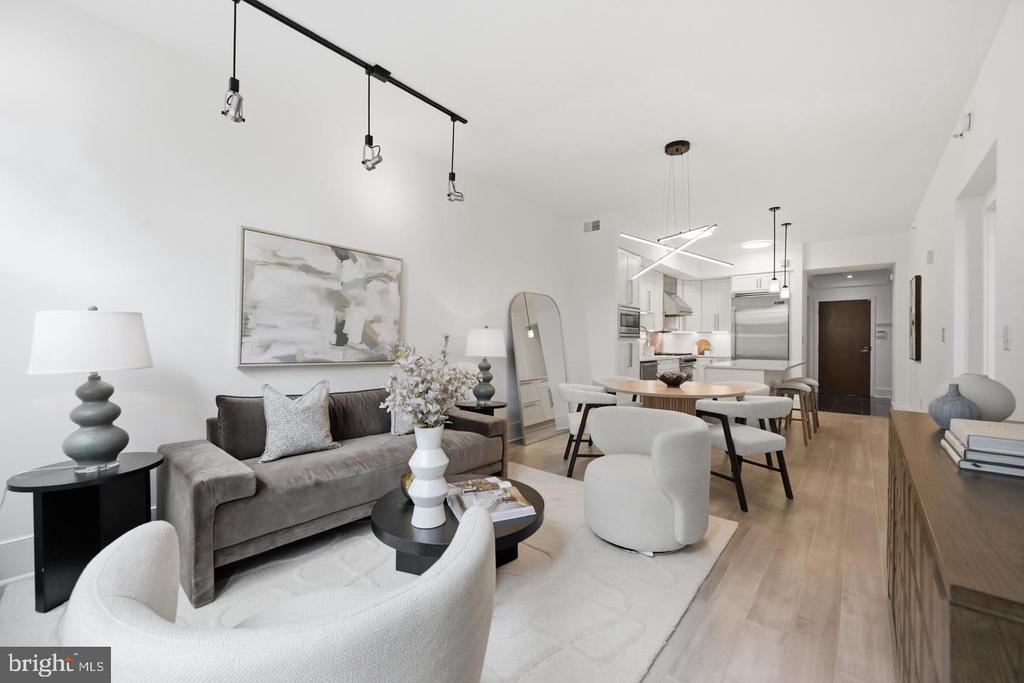 Staged open-plan living room with gray sofa, white chairs, and the kitchen beyond.