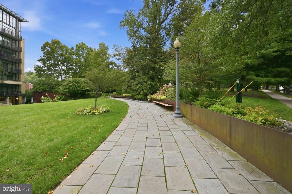Landscaped residential grounds with a curving stone walkway, lawn, mature trees, and apartment building.