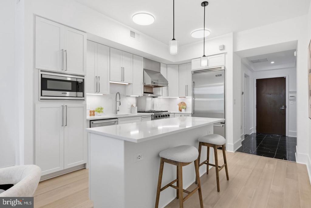 Modern white kitchen with a large island, stainless steel appliances, and two bar stools.