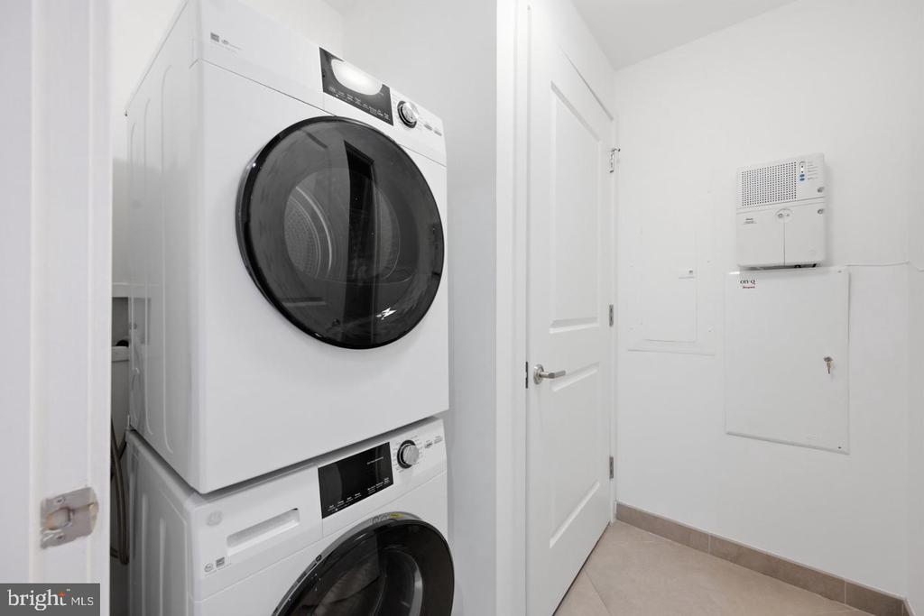 Stacked white front-loading washer and dryer in a bright laundry room beside a paneled door.