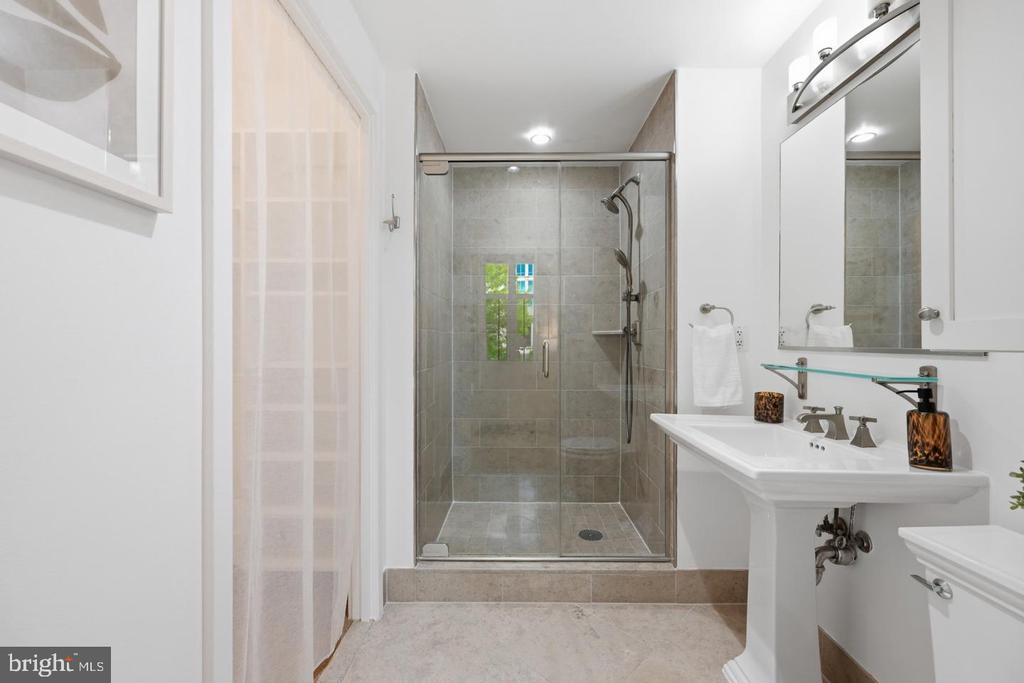 Bathroom with a glass-enclosed tiled shower, pedestal sink, and large mirror.