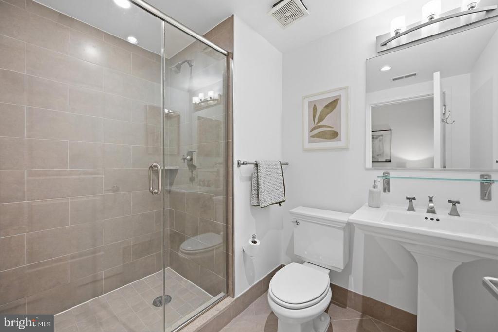 Bathroom with a beige-tiled glass shower, white toilet, and pedestal sink beneath a wide mirror.