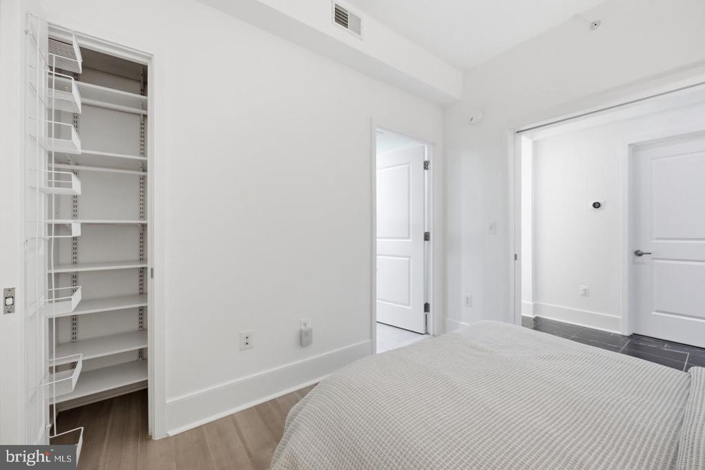 Bedroom with an open wire-shelved closet and a bed in the foreground.