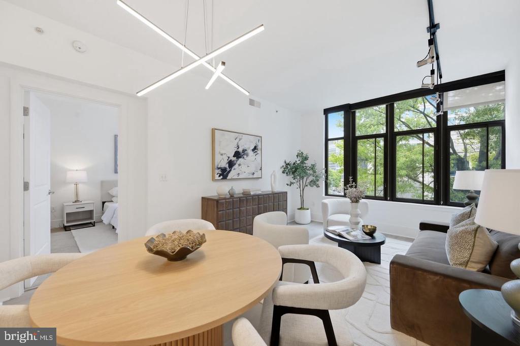 Open-plan living and dining room with a wood table, gray sofa, and large black-framed windows.