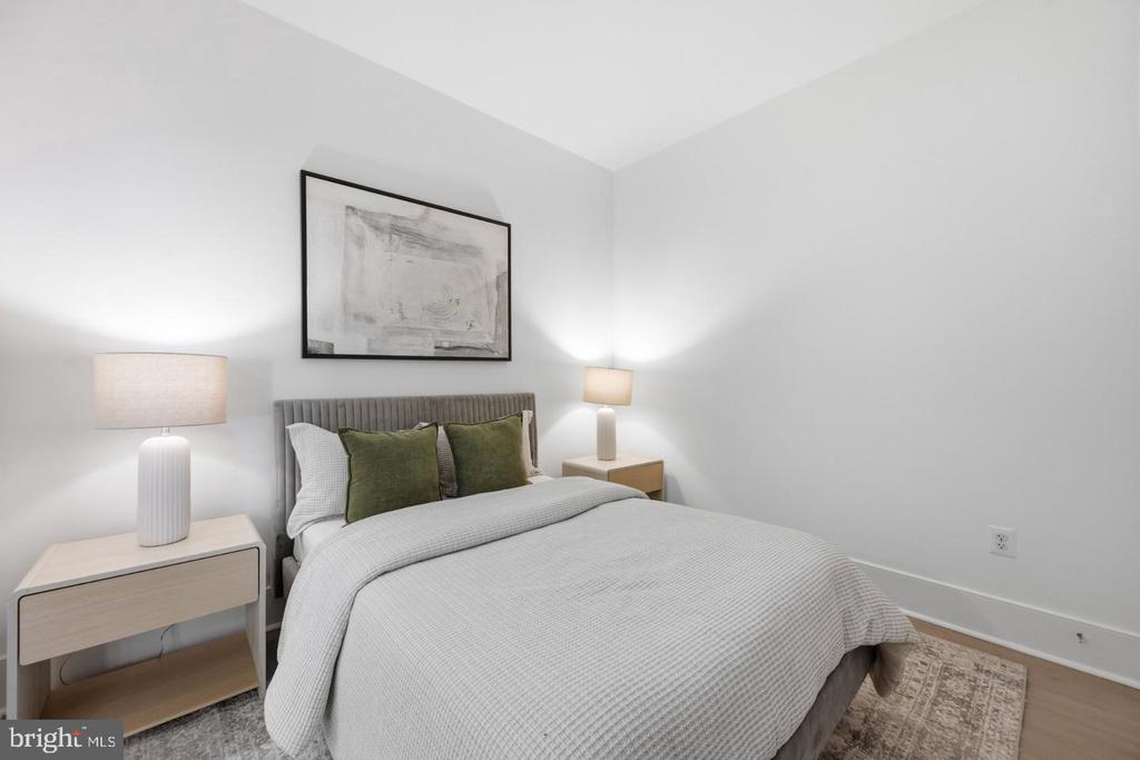 Staged bedroom with a gray upholstered bed, green pillows, and light-wood nightstands.