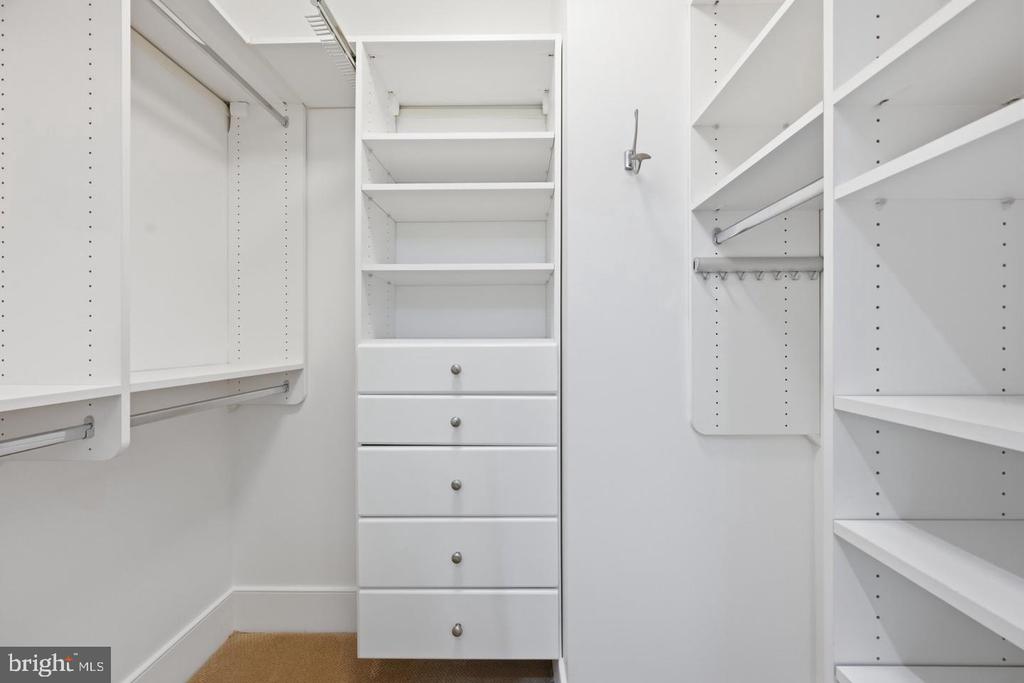 Walk-in closet with white built-in shelves, hanging rods, and a central stack of drawers.